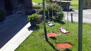 A wooden house with a swing set in a grassy yard.