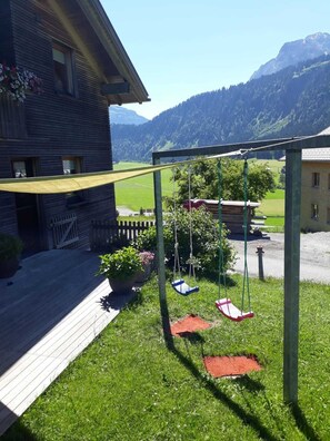 A wooden house with a swing set in a grassy yard.