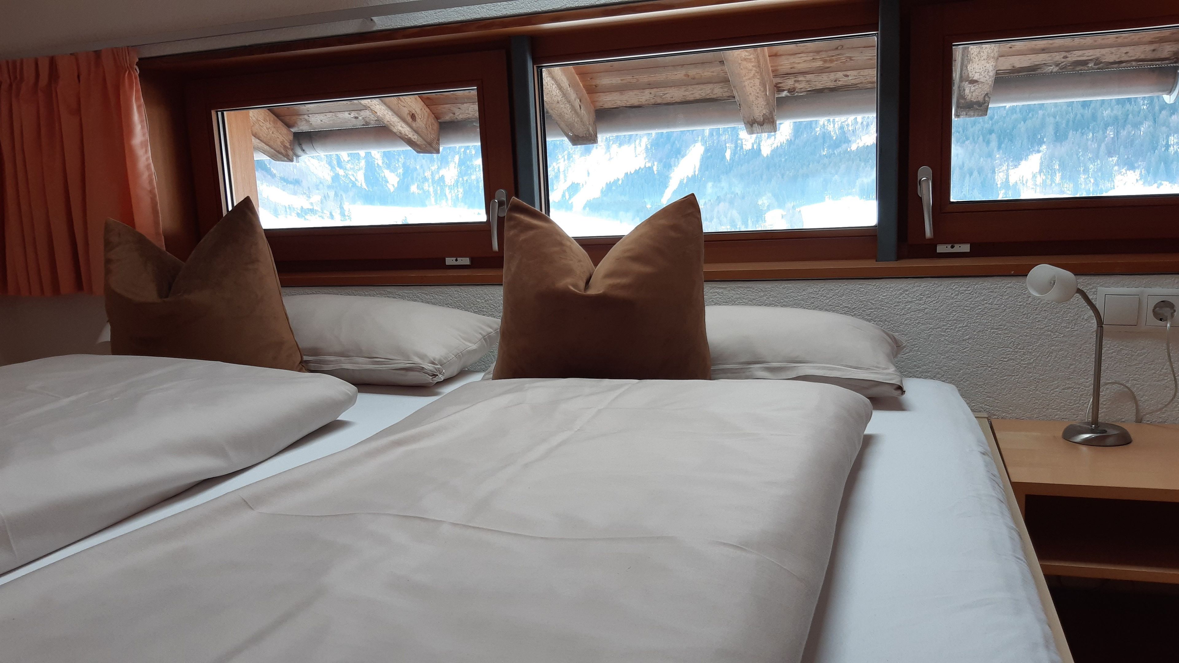 Une chambre avec deux lits, une tête de lit en bois, une table de chevet avec une lampe et une fenêtre donnant sur la montagne.