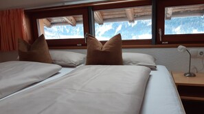 A bedroom with two beds, wooden headboard, a nightstand with a lamp, and a window with a mountain view.