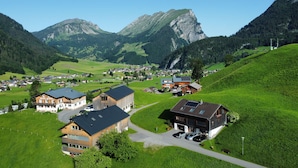 A mountainous village with traditional wooden houses, a central building with a sloped roof, and a clear view of the surrounding hills.