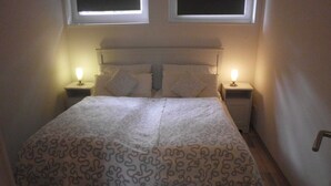 A neatly made bed with a patterned bedspread, two bedside lamps, and a window above the bed. - VV 32; 2-space; 1ST FLOOR; Balcony; 38m² - Villa Vogelsang (Sierksdorf)