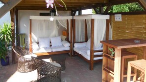A covered outdoor seating area with two cushioned benches, wicker chairs, and a wooden table. - VV 32; 2-space; 1ST FLOOR; Balcony; 38m² - Villa Vogelsang (Sierksdorf)