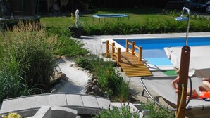 A pool area with a wooden deck, lounge chairs, and a small garden with potted plants. - VV 32; 2-space; 1ST FLOOR; Balcony; 38m² - Villa Vogelsang (Sierksdorf)