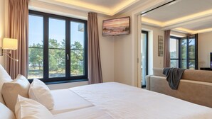 A hotel room with a large bed, a sofa, a TV, and a view of trees. - Nice apartment in Binz with house sea view (Prora/Rügen)