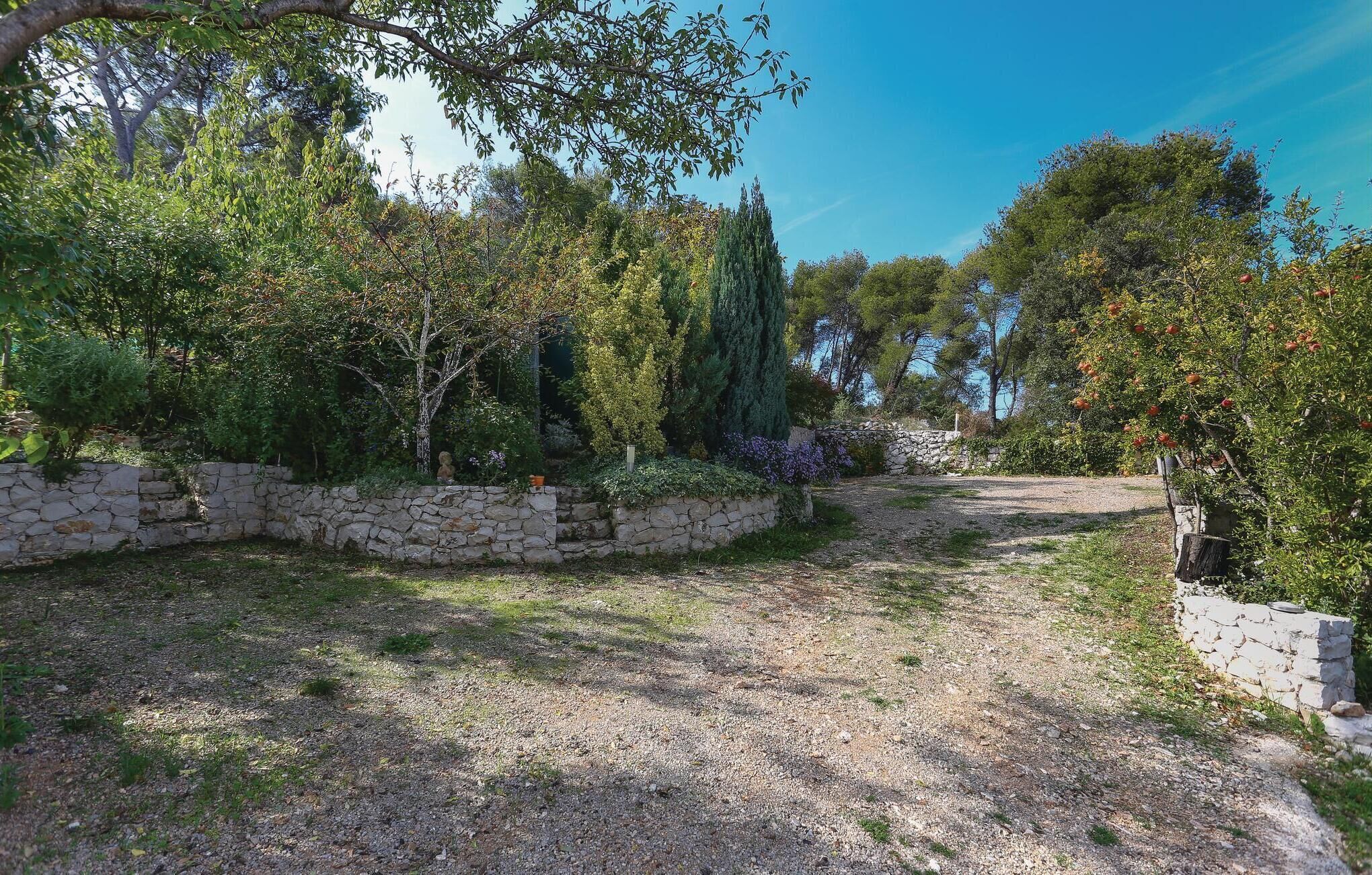 Ein Kiesweg schlängelt sich durch einen Garten mit Steinmauern und verschiedenen Bäumen.