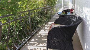 A balcony with a metal railing, a small table with a chair, and a window overlooking a garden. - Gorgeous apartment in Arbanija with WiFi (Arbanija)