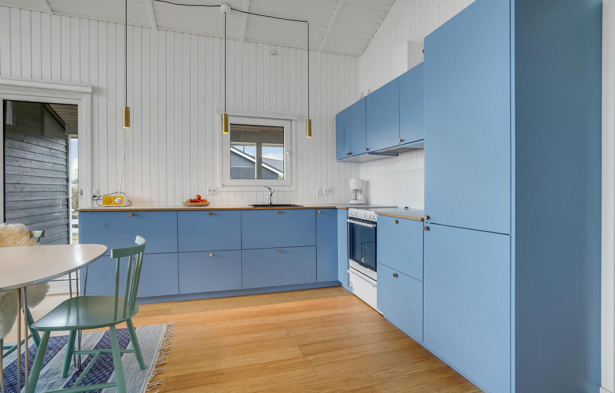 A modern kitchen with blue cabinets, a wooden floor, and a dining area with a table and chairs.