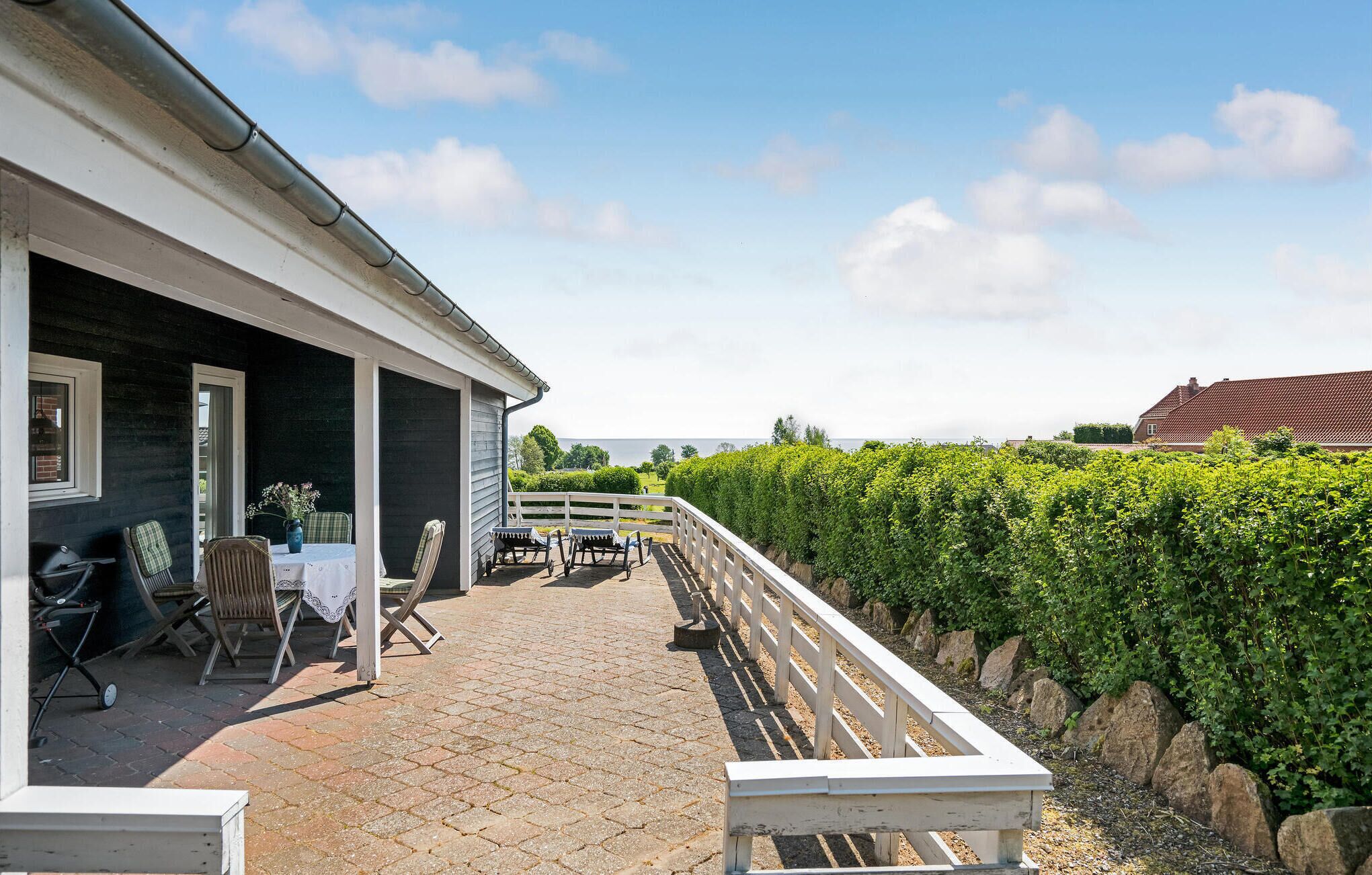 En overdækket terrasse med et bord, stole, grill og udsigt over en vingård.