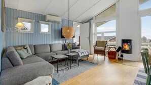 Una sala moderna con un sofá seccional gris, una pequeña mesa de centro, una silla de mimbre y una chimenea.