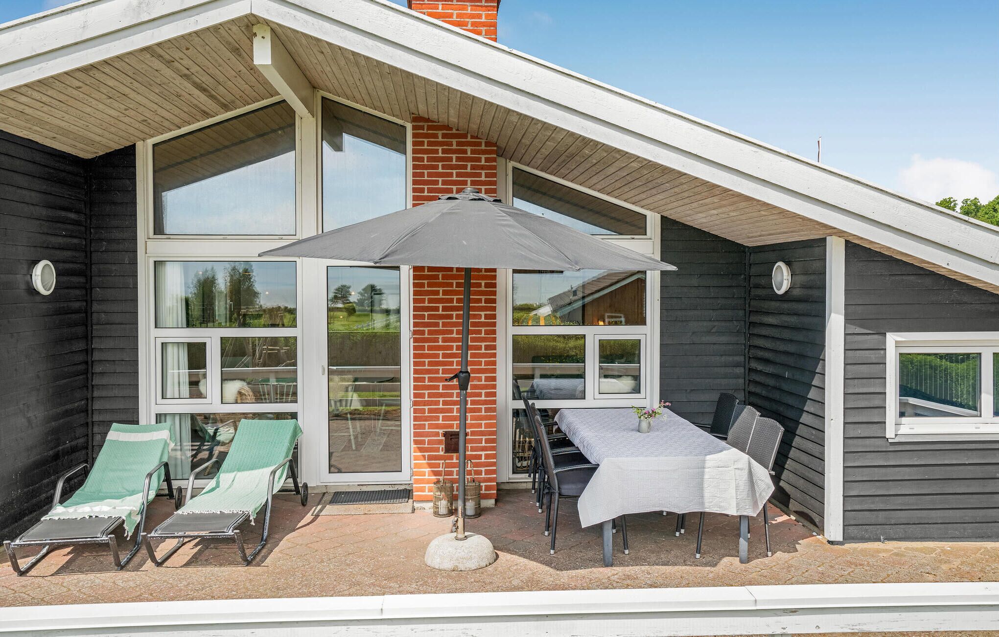 A modern house with a patio area featuring a table and chairs, a covered seating area, and a large window.