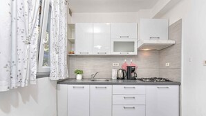 A modern kitchen with white cabinets, a stainless steel sink, a gas stove, and a microwave. - Holiday apartment mit Klimaanlage und Terrasse (Porec)