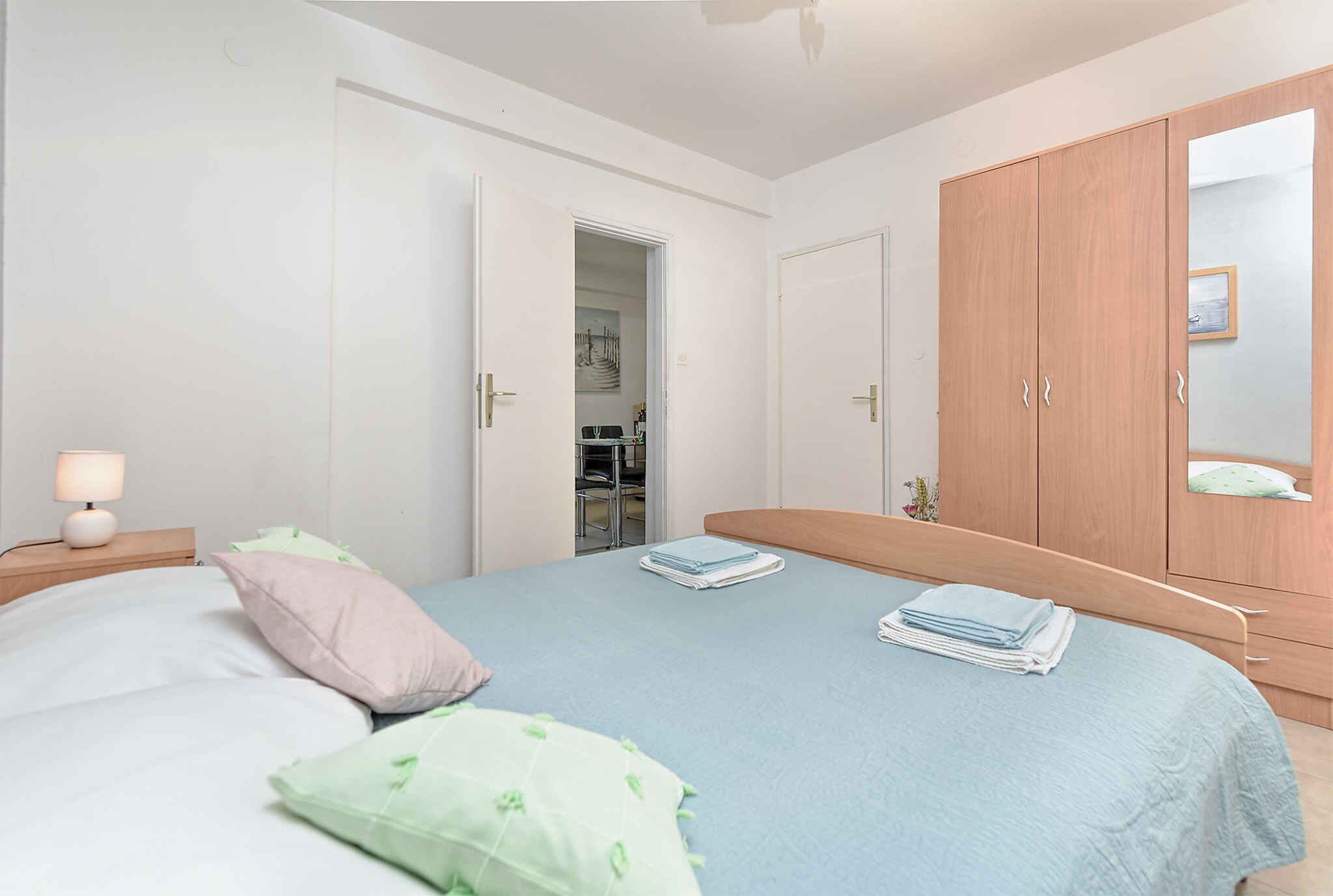 A bedroom with a bed, pillows, a nightstand, a wardrobe, and a mirror.