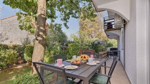 An outdoor patio with a table set for dining, surrounded by greenery and a stone wall. - Holiday apartment mit Klimaanlage und Terrasse (Porec)