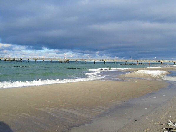 Une plage avec une jetée qui s’avance dans l’eau, un ciel nuageux et des vagues qui se rapprochent du rivage.