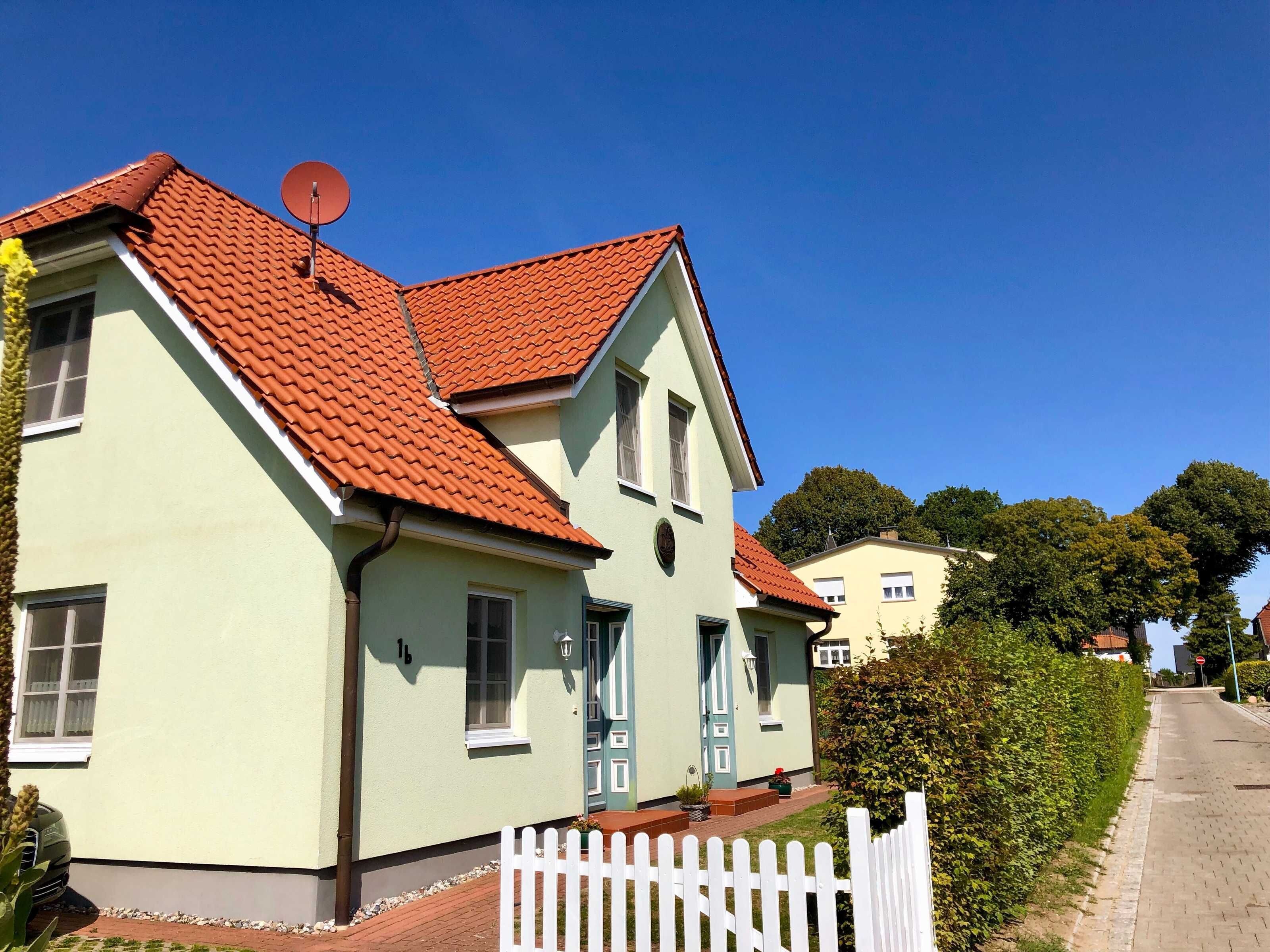 Ein zweigeschossiges Haus mit rotem Ziegeldach, einer Sat-Schüssel und einem weißen Zaun.