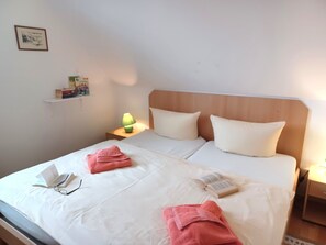 Ein Doppelbett mit weißen Leinen, zwei Kissen, eine Nachttischlampe und ein Nachttisch mit Lampe und Büchern.