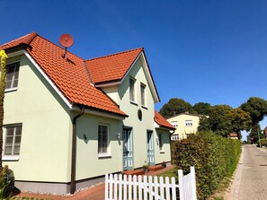 Ein zweigeschossiges Haus mit rotem Ziegeldach, einer Sat-Schüssel und einem weißen Zaun.