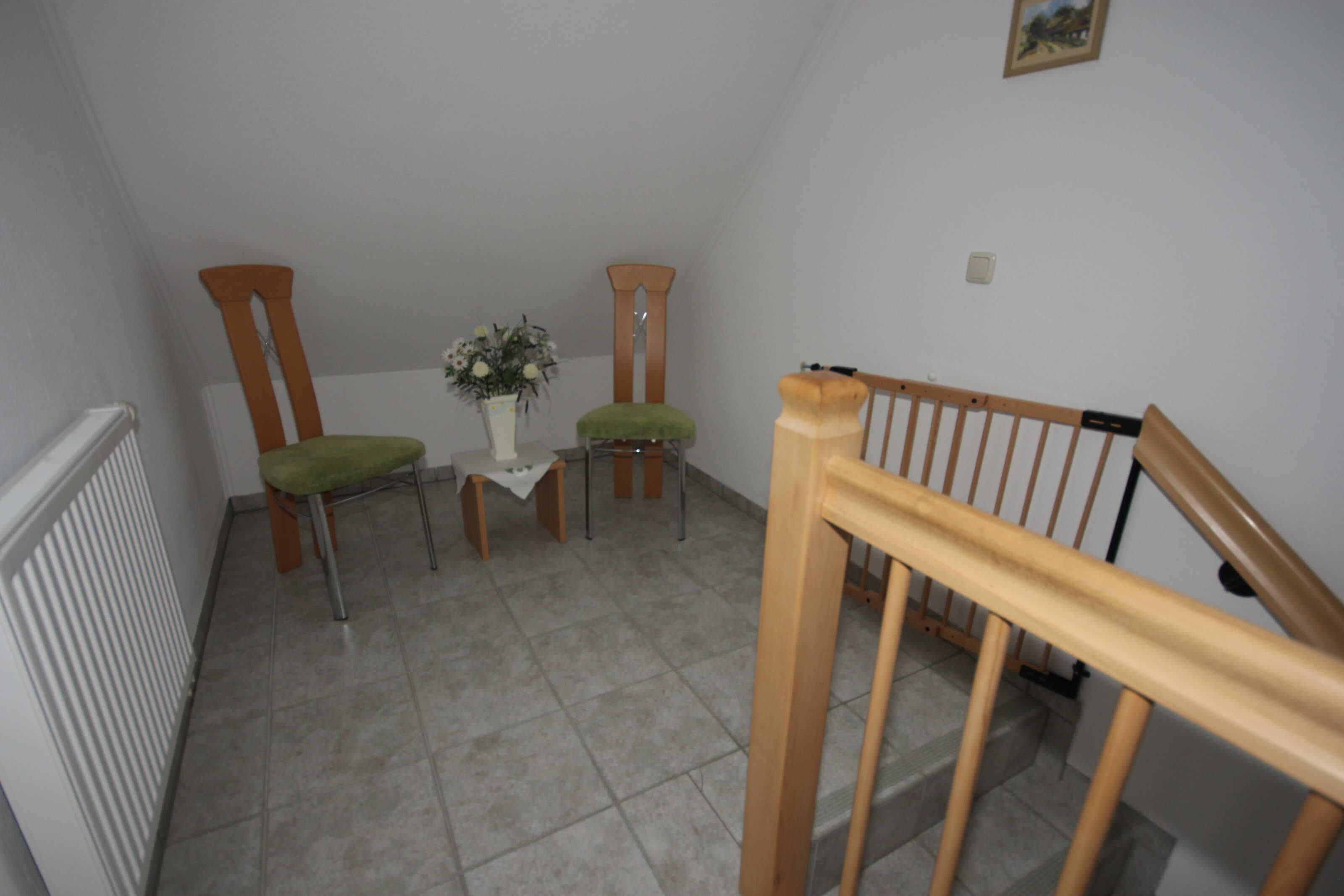 A room with a wooden chair, a small table with a vase, and a staircase with a wooden railing.