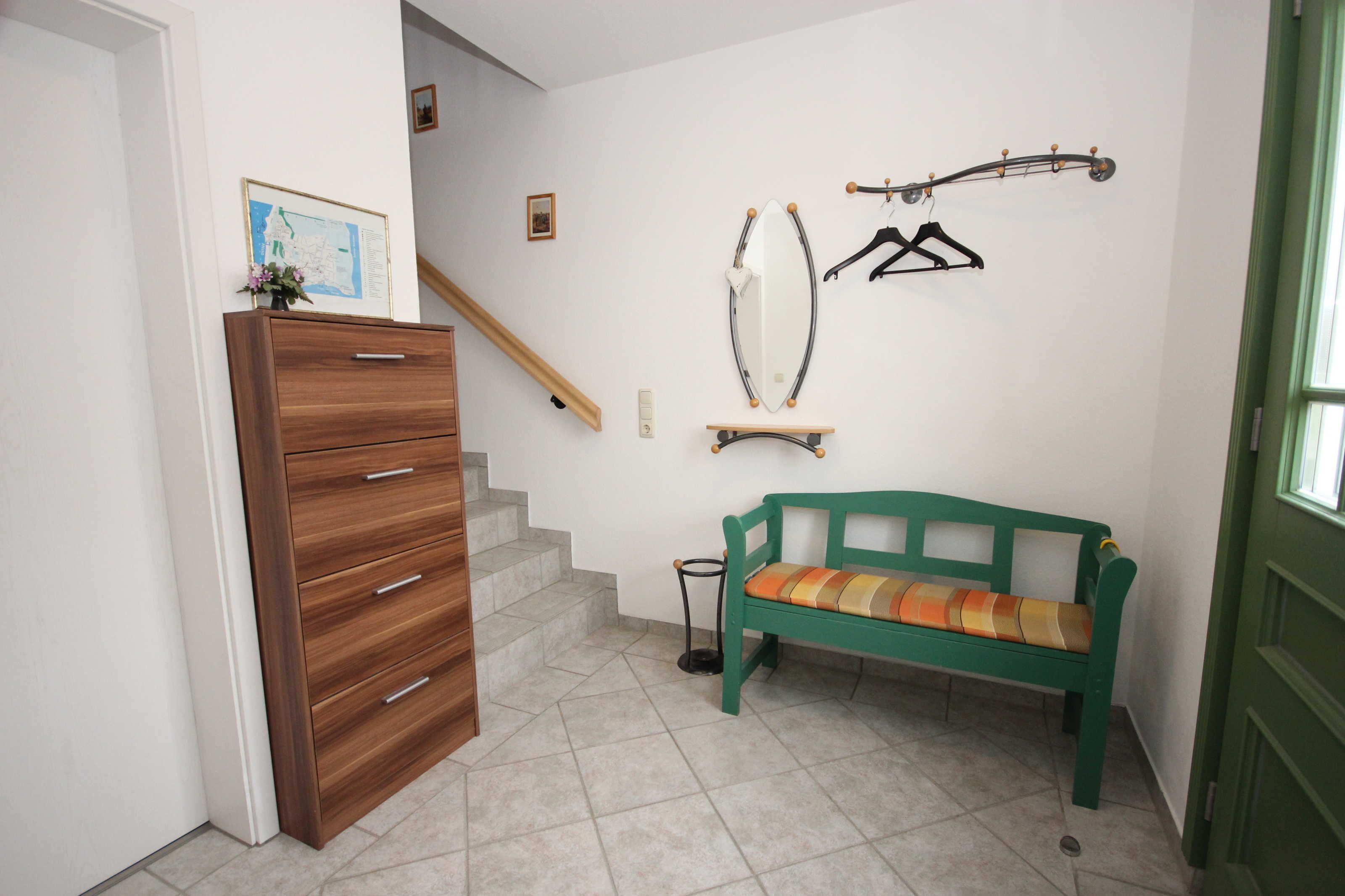 A staircase leading to a second floor, a wooden dresser, a bench with a cushion, a mirror, and a coat rack.