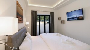 Habitación de hotel con cama, cabecero, televisor montado en la pared, un cuadro y vistas por la ventana.
