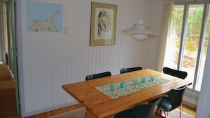 Ein Essbereich mit Holztisch, grünen Stühlen, einer Spitzen Tischdecke und gerahmten Kunstwerken an der Wand.