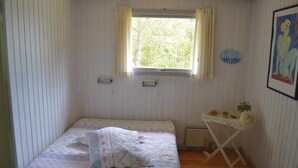Ein kleines Zimmer mit einem Einzelbett, einem Fenster, einer Heizung und einem Tisch mit einer Pflanze.