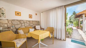 A cozy room with a stone wall, yellow furniture, and a table with a yellow tablecloth. There are framed pictures on the wall and a view of the garden outside. - Studio with 20sqm terrace near the city centre (Baška)