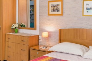 A bedroom with a wooden wardrobe, a bedside table with a lamp, a bed with white bedding, and a wall-mounted picture frame. - Studio with 20sqm terrace near the city centre (Baška)