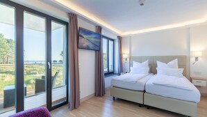 A hotel room with two beds, a large window with a view of the outdoors, a painting on the wall, and a small table with a lamp. - Luxurious apartment in Binz with indoor swimming pool (Prora/Rügen)