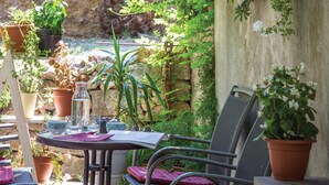 Eine Terrasse mit Tisch für zwei Personen, umgeben von Blumentöpfen und einer Steinmauer.