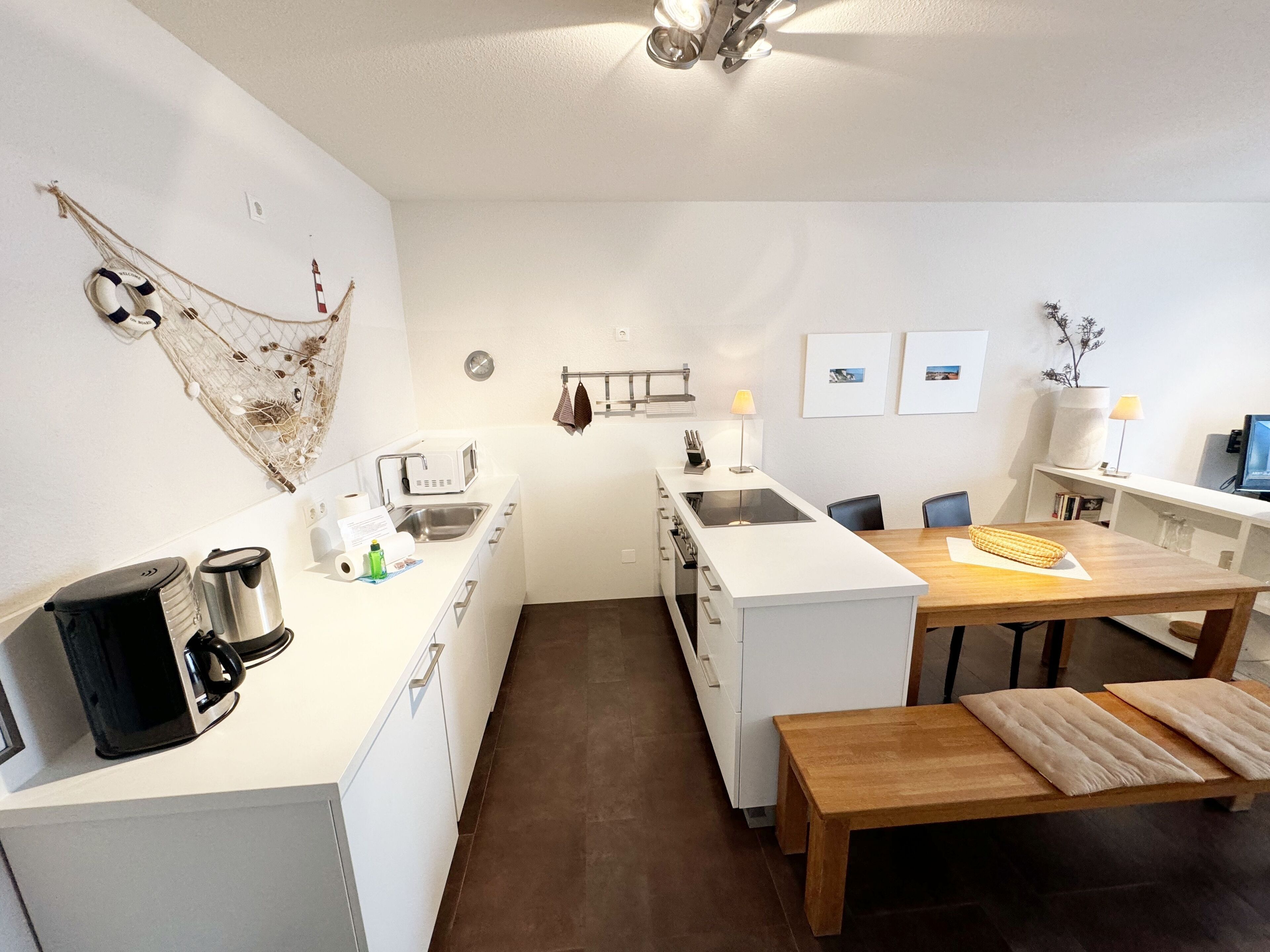 Eine kleine Küche mit weißen Schränken, einer Kaffeemaschine, einem Spülbecken und einem Essbereich mit einem Holztisch und Stühlen.