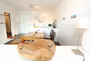 A modern kitchen with a dining table, chairs, and a unique wooden centerpiece. - F: Apartment Düne No. 09 - A jewel for your vacation! - Vacation apartment Düne (Thiessow)