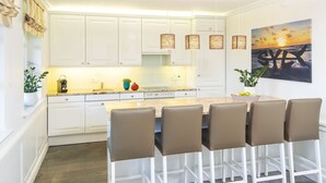 Uma cozinha moderna com armários brancos, uma ilha central e banquetas de bar.