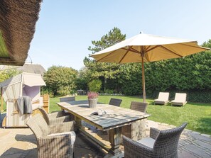 An outdoor patio with a table and chairs, a large umbrella, and a thatched structure.
