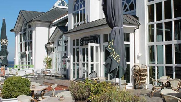 A seaside restaurant with outdoor seating, a sign reading "Seebrücke," and a large "GUINNESS" banner.