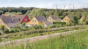 A row of houses with sloped roofs, surrounded by greenery and a forested hill in the background.