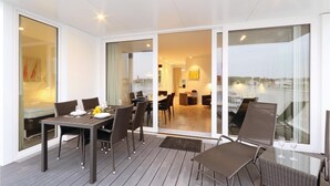 Een modern buitenontbijtgedeelte met een tafel voor twee personen, omringd door rieten stoelen, en een uitzicht op de skyline door grote glazen deuren.