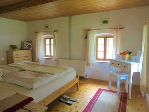 A bedroom with a bed, a desk, a chair, a radiator, and two windows.