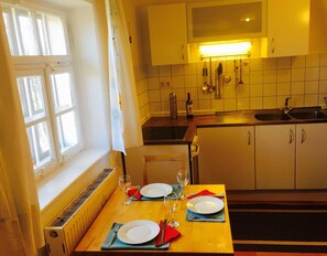A kitchen with a dining table set for two, a window with curtains, and a tiled backsplash.
