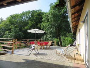 A wooden deck with outdoor furniture, including chairs and a table, under a covered area.