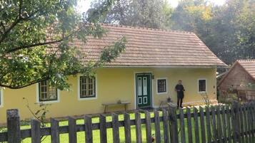 Une maison jaune avec une porte verte, une clôture en bois et une personne debout dans la cour.
