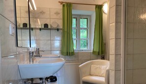A bathroom with a white sink, a mirror, green curtains, and a white radiator.
