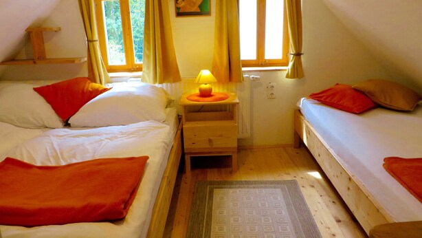 Ein Zimmer mit zwei Betten, einem Nachttisch mit Lampe, einem Fenster mit Vorhängen und einem Gemälde an der Wand.