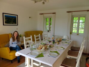 A dining area with a table set for four, chairs, a yellow armchair, and a window with curtains.