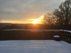 A snowy landscape with a sunset, a wooden fence, and trees in the background.