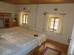 A bedroom with a bed, two windows with curtains, a radiator, and a wooden wardrobe.