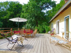 A wooden deck with outdoor furniture, including chairs and a table, surrounded by lush greenery.
