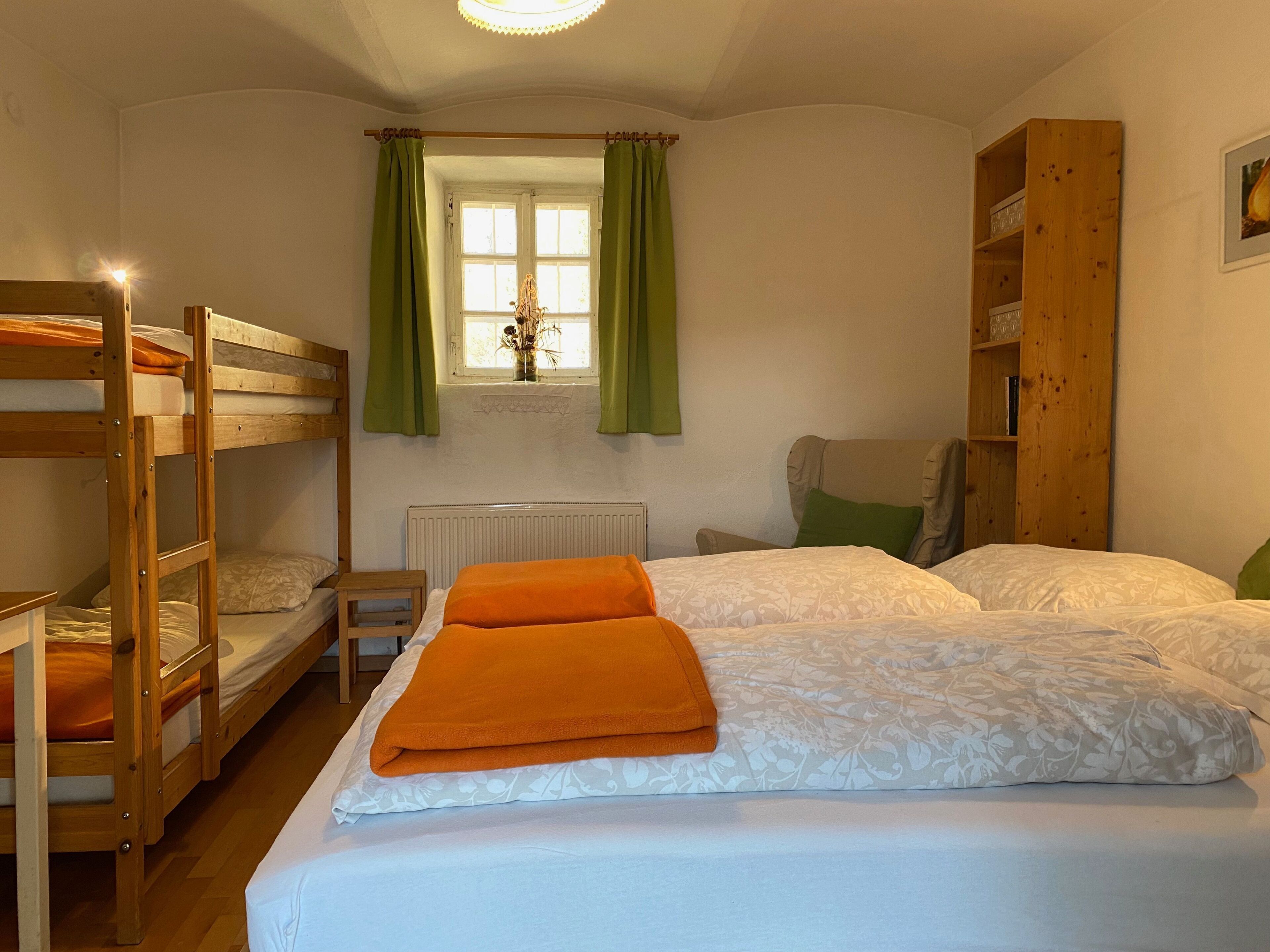 Une pièce avec des lits superposés, un radiateur, une fenêtre avec des rideaux et une bibliothèque en bois.