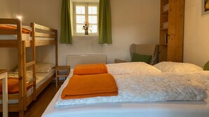A room with bunk beds, a radiator, a window with curtains, and a wooden bookshelf.